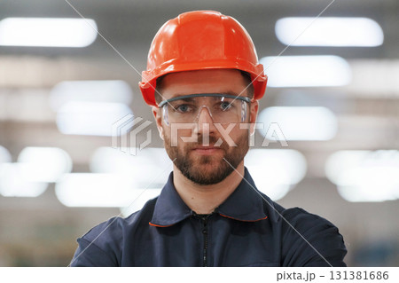 Focused portrait, in glasses. Factory worker is indoors with hard hat Focused portrait, in glasses. Factory worker is indoors with hard hat 131381686