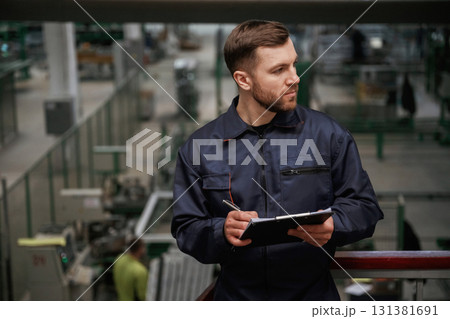 Writing information into the notepad. Factory worker is indoors with hard hat Writing information into the notepad. Factory worker is indoors with hard hat 131381691