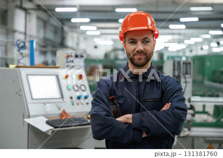 Standing with arms crossed. Factory worker is indoors with hard hat Standing with arms crossed. Factory worker is indoors with hard hat 131381760