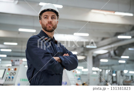 Posing, with arms crossed. Factory worker is indoors with hard hat Posing, with arms crossed. Factory worker is indoors with hard hat 131381823