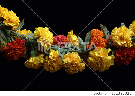 Yellow and orange marigolds are woven into a garland. Black background. 131382320