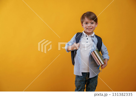 Ready for the school, holding books. Little boy is in the studio against yellow background Ready for the school, holding books. Little boy is in the studio against yellow background 131382335