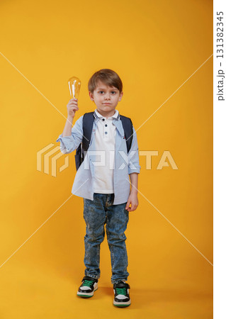 Light bulb in hand. Conception of smart person and idea. Little boy is in the studio against yellow background 131382345