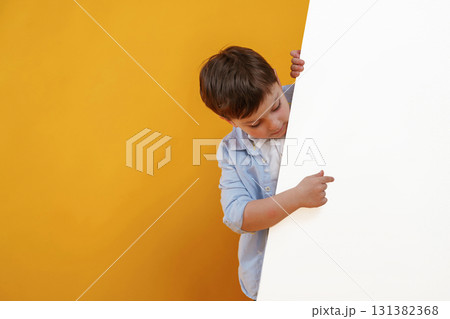 Showing something on the blank white surface. Little boy is in the studio against yellow background Showing something on the blank white surface. Little boy is in the studio against yellow background 131382368