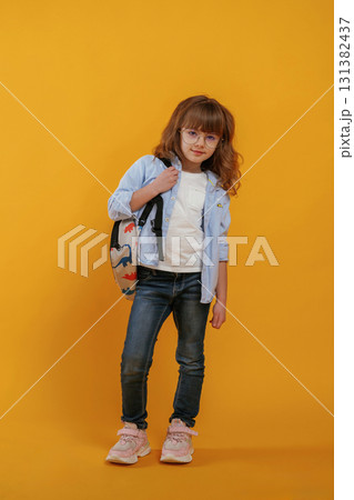With backpack. Cute little girl is against yellow background With backpack. Cute little girl is against yellow background 131382437
