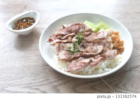 grilled slice pepper beef meat brisket with cucumber and fried crispy garlic topping plain rice on plate dipping Thai spicy sauce grilled slice pepper beef meat brisket with cucumber and fried crispy garlic topping plain rice on plate dipping Thai spicy sauce 131382574