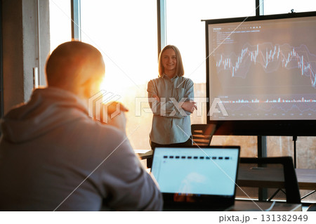 Beautiful sun beam. Female business trainer is against projector with business data, teaching the man Beautiful sun beam. Female business trainer is against projector with business data, teaching the man 131382949