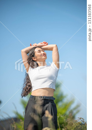 青空の下で音楽を聴きながら運動するロングヘアの若い女性 青空の下で音楽を聴きながら運動するロングヘアの若い女性 131383568