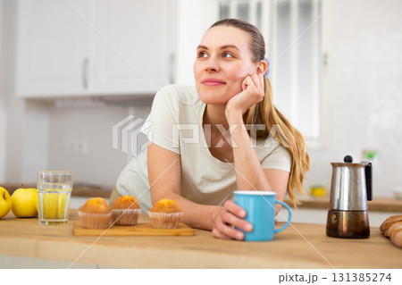 Happy young woman enjoying cupcakes with coffee in kitchen 131385274