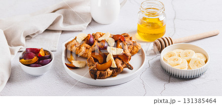 Sweet croffles with banana, plum and honey on a plate on the table web banner 131385464