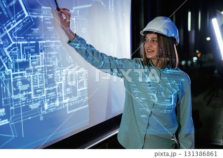 In white hard hat. Female architect is showing construction site plan for building on projector 131386861