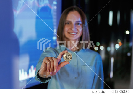 Close up of digital currency coin in hand. Businesswoman is against projector with graphs, indoors Close up of digital currency coin in hand. Businesswoman is against projector with graphs, indoors 131386880