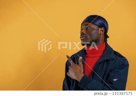 Pointing by the finger to copy space. Handsome black man is in the studio against yellow background Pointing by the finger to copy space. Handsome black man is in the studio against yellow background 131387171