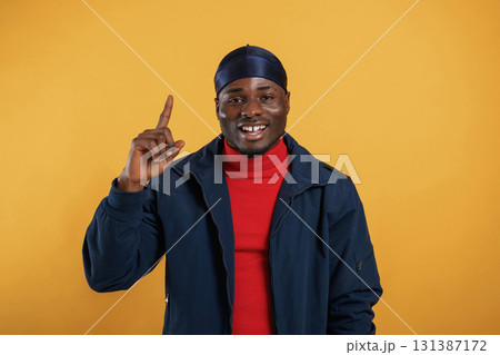 Pointing by the finger to copy space. Handsome black man is in the studio against yellow background 131387172