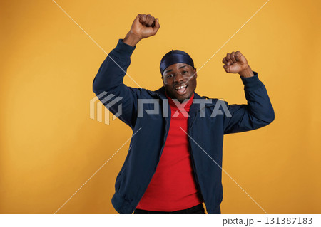 Having fun, celebrating success, hands up. Handsome black man is in the studio against yellow background 131387183