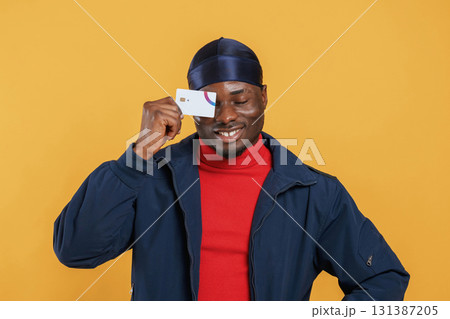 Covering eye by credit card. Handsome black man is in the studio against yellow background Covering eye by credit card. Handsome black man is in the studio against yellow background 131387205