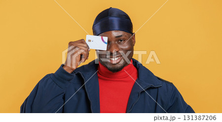 Covering eye by credit card. Handsome black man is in the studio against yellow background Covering eye by credit card. Handsome black man is in the studio against yellow background 131387206