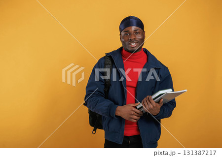 Student with books, backpack and notepad. Handsome black man is in the studio against yellow background Student with books, backpack and notepad. Handsome black man is in the studio against yellow background 131387217
