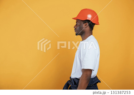 Standing and posing, construction worker in hard hat. Handsome black man is in the studio against yellow background 131387253
