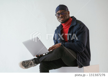 Front view, with laptop. Black man in cap is in the studio against white background Front view, with laptop. Black man in cap is in the studio against white background 131387276