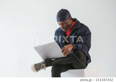 Front view, with laptop. Black man in cap is in the studio against white background 131387282