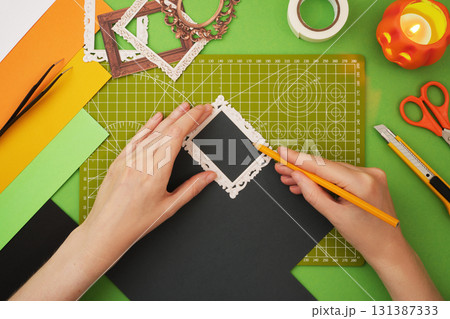 Making a Halloween craft. Hands draw the outline of the ghosts portrait. 131387333