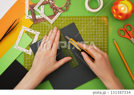 Making a Halloween craft. Hands cutting grey paper with a ruler and utility knife on a grid cutting mat 131387334