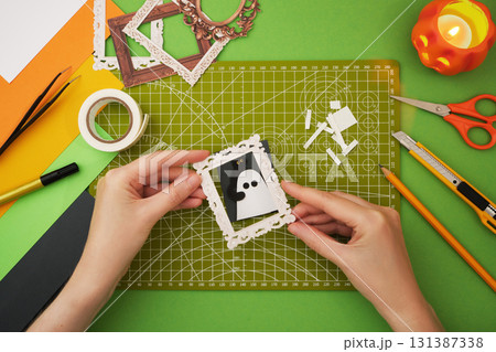 Making a Halloween craft. Hands glue the frame to the ghost portrait. 131387338