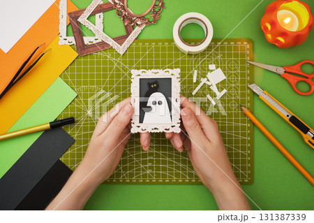 Making a Halloween decoration. Hands holding a small Halloween craft picture with a ghost and black cat Making a Halloween decoration. Hands holding a small Halloween craft picture with a ghost and black cat 131387339