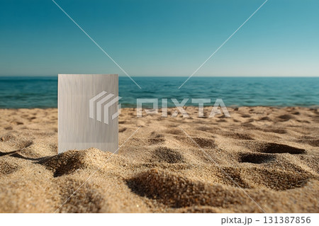 A blank white board stands on a sandy beach facing the ocean. 131387856