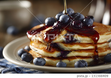 Blueberry pancakes are stacked high and covered with syrup and fresh berries. 131388409
