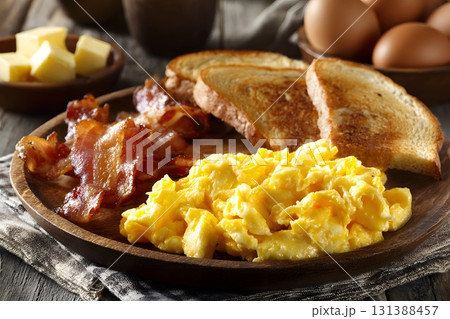 American breakfast plate with scrambled eggs, bacon, and toast on a wooden table. American breakfast plate with scrambled eggs, bacon, and toast on a wooden table. 131388457