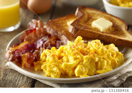 A plate of scrambled eggs with bacon and toast sits ready to eat. A plate of scrambled eggs with bacon and toast sits ready to eat. 131388458