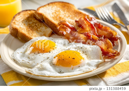 Two fried eggs and crispy bacon sit beside toast. Two fried eggs and crispy bacon sit beside toast. 131388459