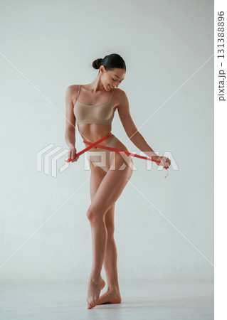 With measuring tape. Woman with slim body shape is posing against background With measuring tape. Woman with slim body shape is posing against background 131388896