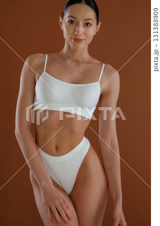 In white underwear. Woman with slim body shape is posing against background In white underwear. Woman with slim body shape is posing against background 131388909