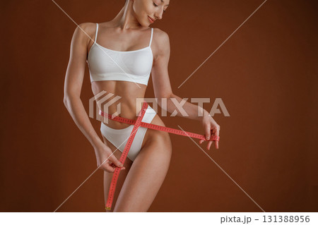 Dieting conception, with measuring tape. Woman with slim body shape is posing against background Dieting conception, with measuring tape. Woman with slim body shape is posing against background 131388956