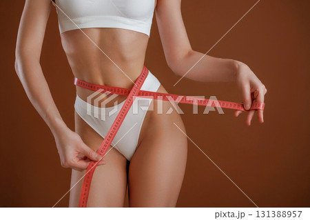 Dieting conception, with measuring tape. Woman with slim body shape is posing against background 131388957