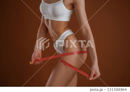 Measuring the leg, conception of weight loss. Woman with slim body shape is posing against background Measuring the leg, conception of weight loss. Woman with slim body shape is posing against background 131388964