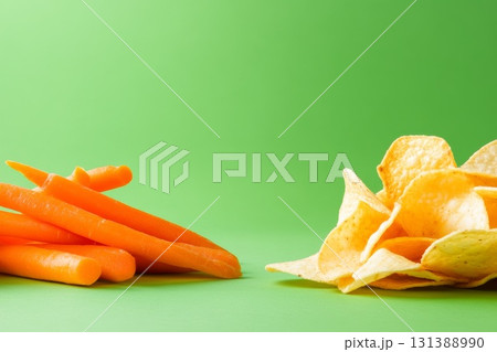 Fresh carrots and crispy potato chips on vibrant green background showcasing healthy versus unhealthy 131388990