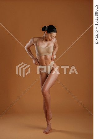 Creamy colored underwear. Woman with slim body shape is posing against background 131389015