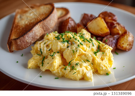 A breakfast plate with scrambled eggs, toast, and potatoes is served. 131389096