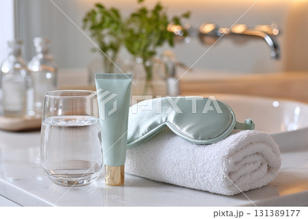 Relaxing sleep tourism setup with skincare products, water, and soft towel on marble countertop 131389177
