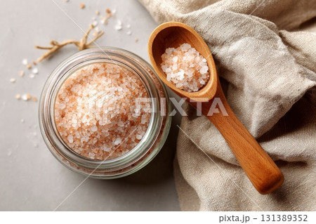 Glass jar filled with pink Himalayan salt beside wooden spoon on textured fabric surface Glass jar filled with pink Himalayan salt beside wooden spoon on textured fabric surface 131389352