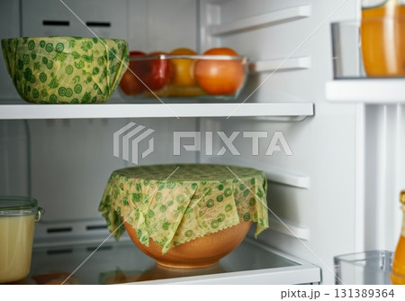 Reusable beeswax wraps covering bowls in a refrigerator showcasing sustainable food storage solutions Reusable beeswax wraps covering bowls in a refrigerator showcasing sustainable food storage solutions 131389364