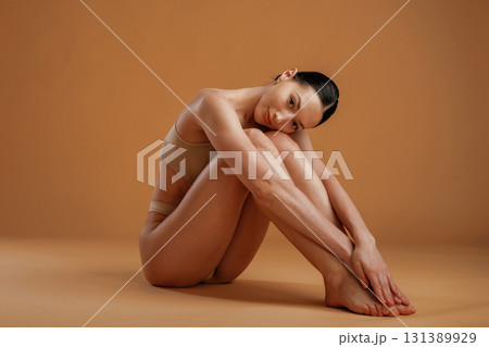 Sitting and resting on the floor. Woman with slim body shape is posing against background 131389929