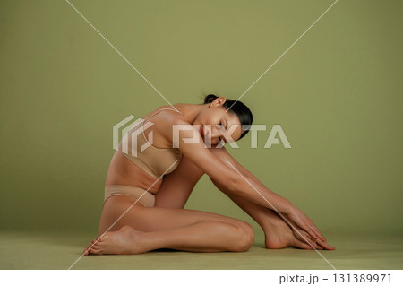 Resting on the floor. Woman with slim body shape is posing against background Resting on the floor. Woman with slim body shape is posing against background 131389971