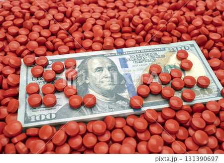 Hundred dollar bill surrounded by numerous red pills, symbolizing intersection of finance and pharmaceuticals. image conveys sense of wealth and health 131390697