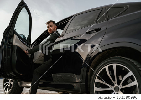 Man in black suit is sitting in the car, opening the door Man in black suit is sitting in the car, opening the door 131390996