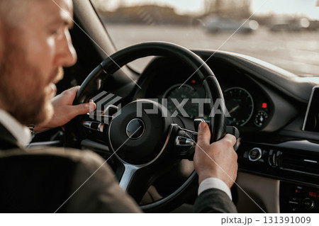 Close up view of steering wheel. Man in black suit is sitting in the car, driving 131391009